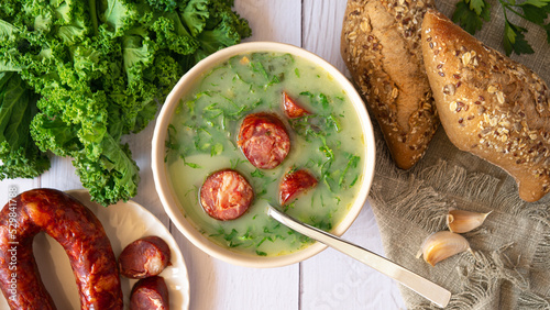 Portuguese style soup called Caldo Verde, bread, Cabbage julienne, and chorizo sausage on a white wooden Table. Flat lay photo