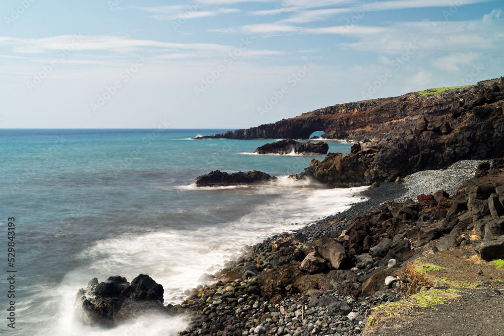 Rocky coastline reveals a view of a sea arch on Maui.