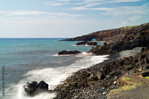 Rocky coastline reveals a view of a sea arch on Maui.