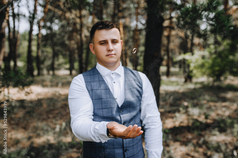 A stylish, young groom tosses a golden ring while standing in a forest in nature. Wedding portrait, photography. A stylish, young groom tosses a golden ring while standing in a forest in nature. Wedding portrait, photography.