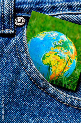 a card with planet Earth - globe - in green grass put in pocket of blue jeans like concept for ecology, enviroment, protection of nature, ecological topics 