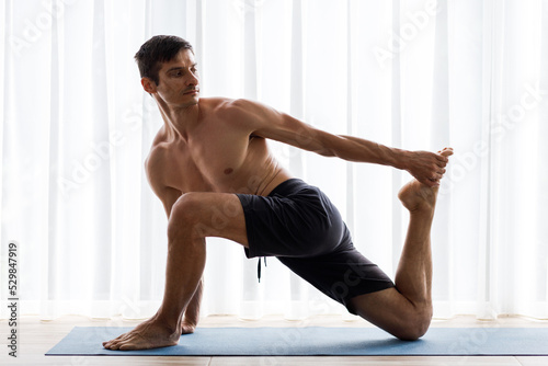 Young sporty man doing stretching legs on yoga mat during morning training