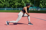 Sportive young woman with long braids takes care of body on summer day. African American lady in sportswear enjoys effective exercise for gluteal muscles on city stadium near park with green trees