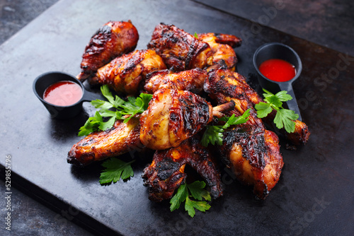Traditional barbecue chicken wings and drumsticks with hot chili mango sauce and coriander served as close-up on a rustic black board