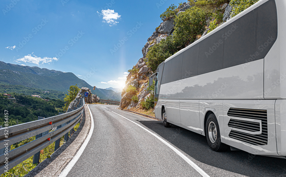 A white tourist bus rides along the highway against the backdrop of a beautiful landscape.