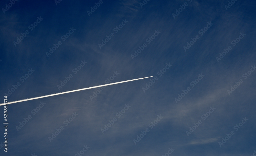 A plane flying in the blue sky and clouds. A white contrail from an airplane in the summer sky. A plane flying in the blue sky and clouds. A white contrail from an airplane in the summer sky.