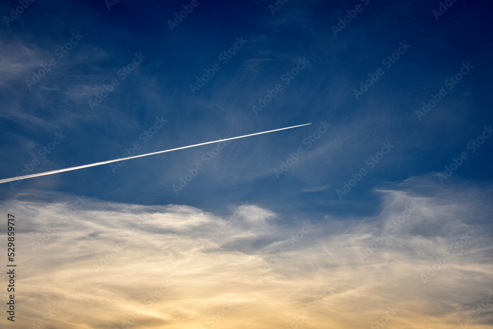 A plane flying in the blue sky and clouds. A white contrail from an airplane in the summer sky. A plane flying in the blue sky and clouds. A white contrail from an airplane in the summer sky.