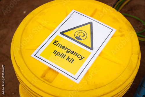 "Emergency spill kit" yellow plastic containment box. Safety sign and symbol at industrial equipment. 
