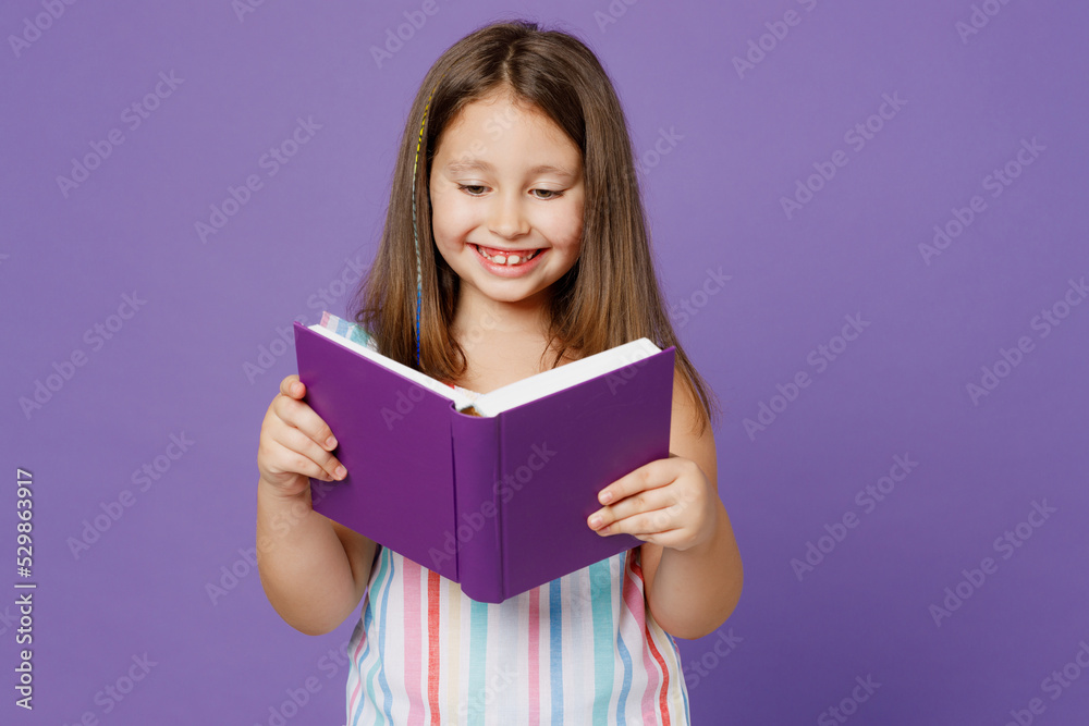 Little smiling smart happy clever fun kid child girl 5-6 years old wears striped dress read book fairy tale isolated on plain pastel light purple background Mother's Day love family lifestyle concept Little smiling smart happy clever fun kid child girl 5-6 years old wears striped dress read book fairy tale isolated on plain pastel light purple background Mother's Day love family lifestyle concept