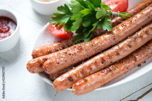 Close-up of grilled sausages with fresh parsley, tomatoes and dips, selective focus, studio shot