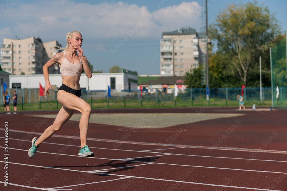Fototapeta premium Young woman running on the running track at the stadium outdoors