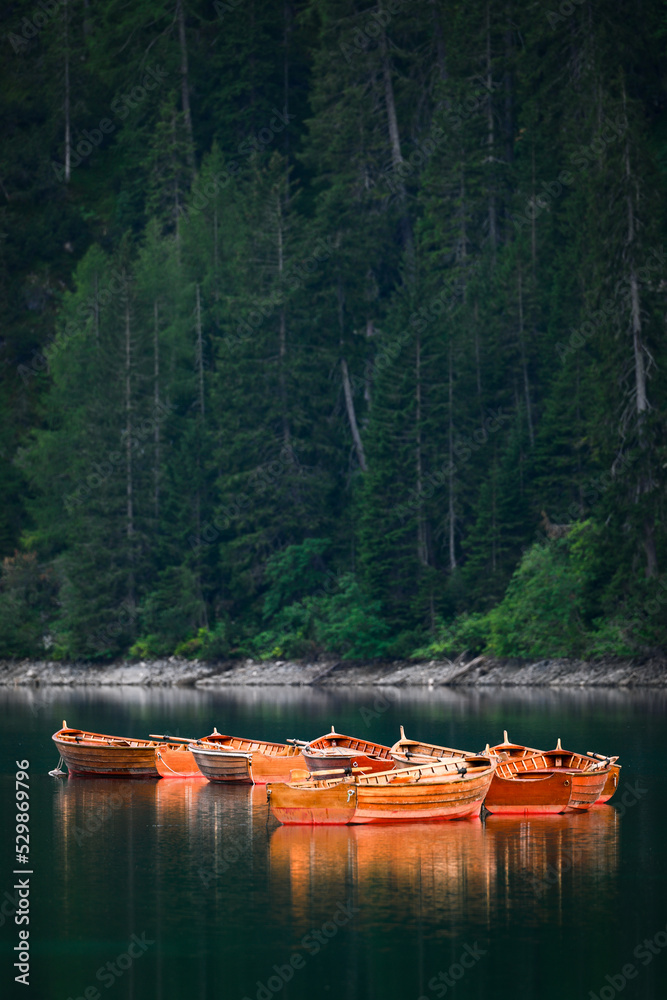 Stunning view of some wooden boats floating on the Lake Braies (Lago di Braies) with a defocused green forest in the background. Lago di Braies is an alpine lake in the Dolomites, Italy
