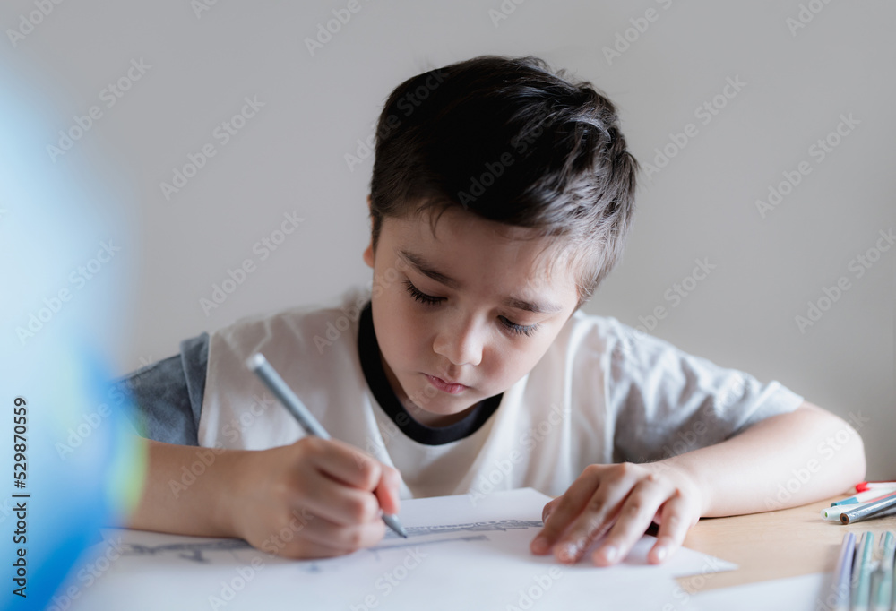 Happy boy using grey colour pen drawing or sketching on paper,Portrait kid siting on table doing homework in living room,Child enjoy art and craft activity at home on weekend,Education concept Happy boy using grey colour pen drawing or sketching on paper,Portrait kid siting on table doing homework in living room,Child enjoy art and craft activity at home on weekend,Education concept