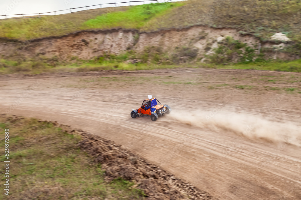A small sports buggy with a child driving on a rally competition track during weekend training on a warm summer day.
