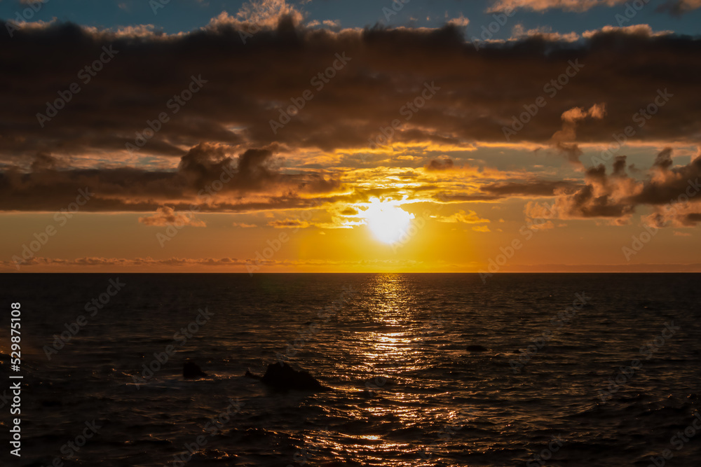 Watching the sunset at the port of Puerto de la Cruz, Tenerife, Canary Islands, Spain, Europe. View of the horizon of Atlantic Ocean. The sun is reflecting in the calm sea. Vibrant clouds in the sky Watching the sunset at the port of Puerto de la Cruz, Tenerife, Canary Islands, Spain, Europe. View of the horizon of Atlantic Ocean. The sun is reflecting in the calm sea. Vibrant clouds in the sky