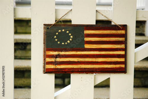 A small Colonial and early American flag decoration hangs from a white picket fence, in a small town, a true sign of Americana on the Fourth of July in the USA photo
