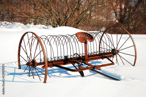 An antique rusted reap stands in the middle of a snow covered field photo