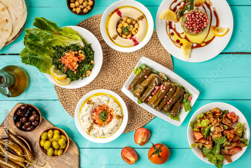 Fototapeta Naklejka Na Ścianę i Meble -  Assorted Arabian food Hommus Beiruti Meat, Baba Ghanouj , olive, chick peas, pita bread Vine Leaves, Tabbouleh, Fattoush, served in dish isolated on wooden table side view of middle eastern food