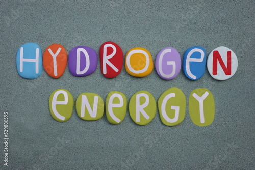 Hydrogen Energy, creative text composed with multi colored stone letters over green sand
