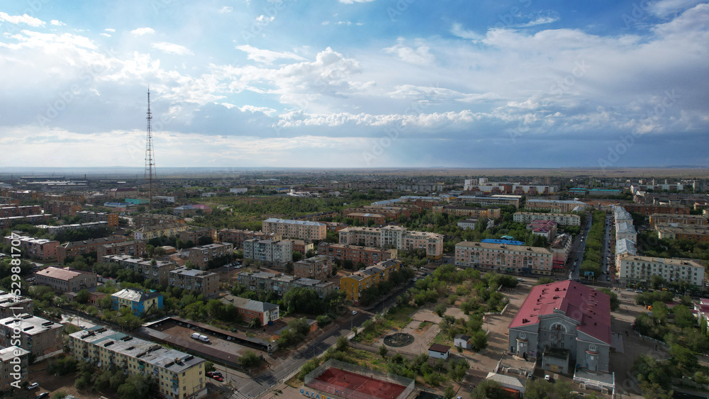 A wet small town after the rain. Big clouds over the city. Rain is visible in the distance. Blue sky in places. Low houses, green parks and roads. There is a TV tower. Balkhash city, Kazakhstan