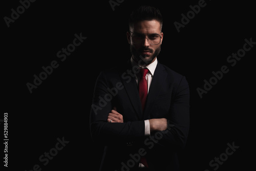 elegant young bearded man in black suit with red tie folding arms