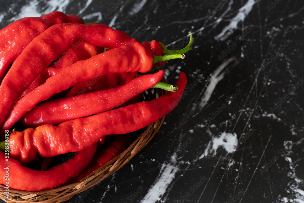 Ripe red peppers in a wicker basket placed on a dark background. A close-up. Top table view. Ripe red peppers in a wicker basket placed on a dark background. A close-up. Top table view.
