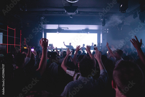 DJ performing in dark nightclub with crowd of people with their hands up