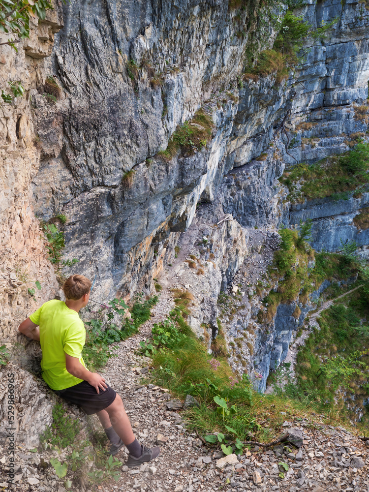 Boy at top of path with steel chain anchored in the rocky wall Boy at top of path with steel chain anchored in the rocky wall