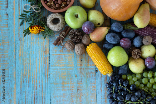 Thanksgiving day table with various fruit (pumpkin, grapes, apple, plum, pear, and nuts) on a rustic wooden background with copy space. Top view. Fresh and healthy autumn food.