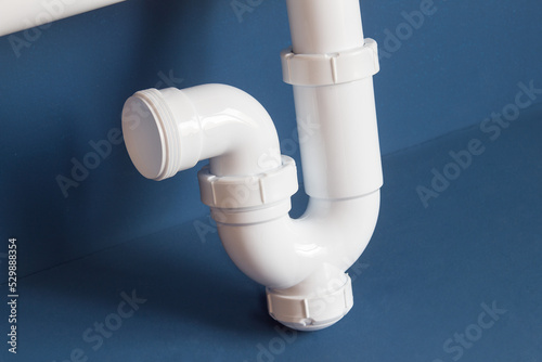 Detail of part of the siphon with a curved pipe with a drain cover on a blue studio background. Objects and maintenance.
