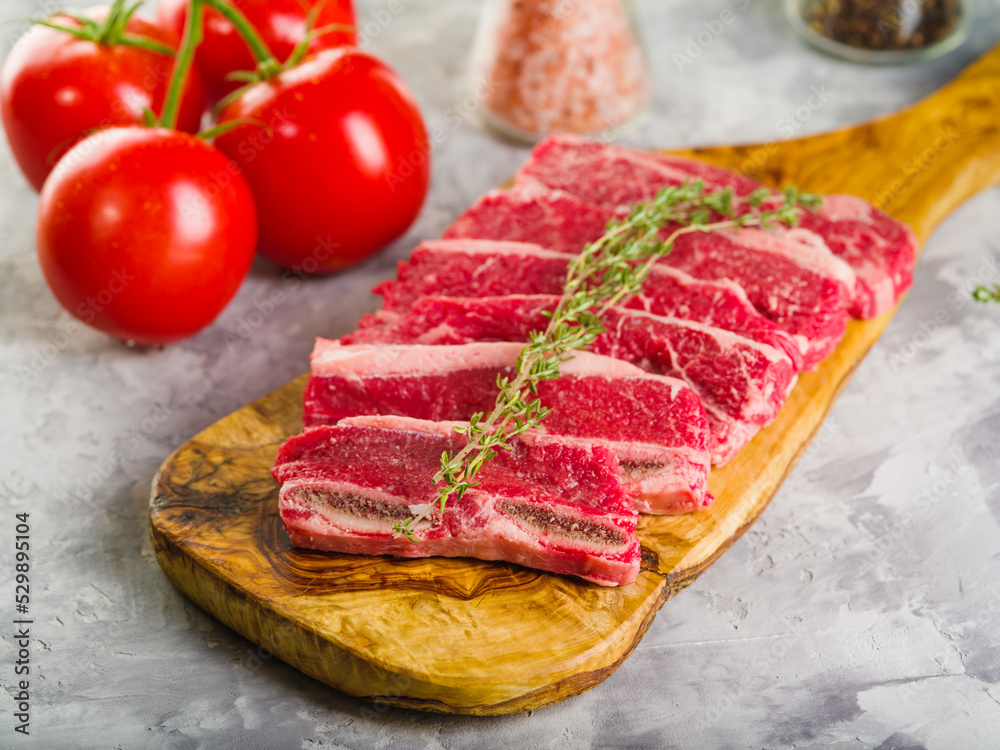 Meat steaks with a sprig of rosemary on a wooden cutting board are waiting to be cooked. Ripe tomatoes, spices on a light background. Home kitchen. Recipes for meat dishes. Meat steaks with a sprig of rosemary on a wooden cutting board are waiting to be cooked. Ripe tomatoes, spices on a light background. Home kitchen. Recipes for meat dishes.