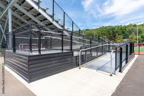 Accessible wheelchair ramp with railings and slip resistant surface at empty metal stadium bleacher.  Nondescript location with no people in image.  Not a ticketed event.  	 photo