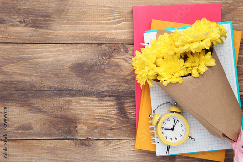 Bouquet of yellow chrysanthemums  notepads and alarm clock on wooden background with copy space. Concept teachers day