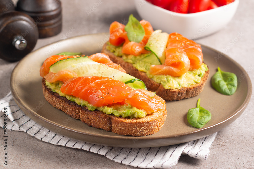 Two tasty open salmon sandwiches with avocado and cucumber. Morning healthy breakfast. Top view. Two tasty open salmon sandwiches with avocado and cucumber. Morning healthy breakfast. Top view.