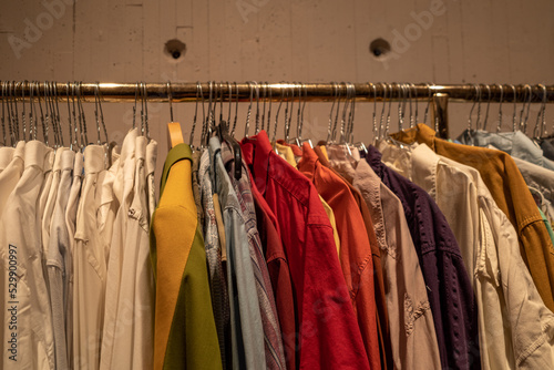 Row of colourful tone fabric and stylish shirts hang on aluminium hanger clothes rack for fitting in retail fashion store or second hand outlet shop.