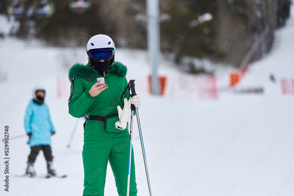 Woman skier in green ski suit looking at smartphone