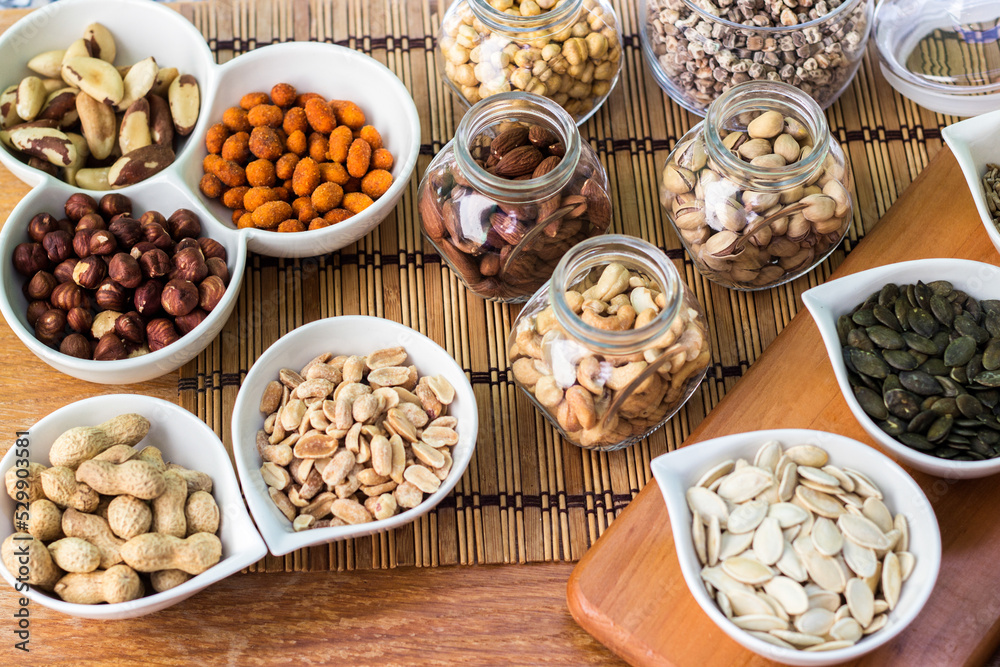 Fototapeta premium Rustic wood table filled with a large assortment of nuts like pistachios, hazelnut, pine nut, almonds, pumpkin seeds, sunflower seeds, peanuts, cashew and walnuts