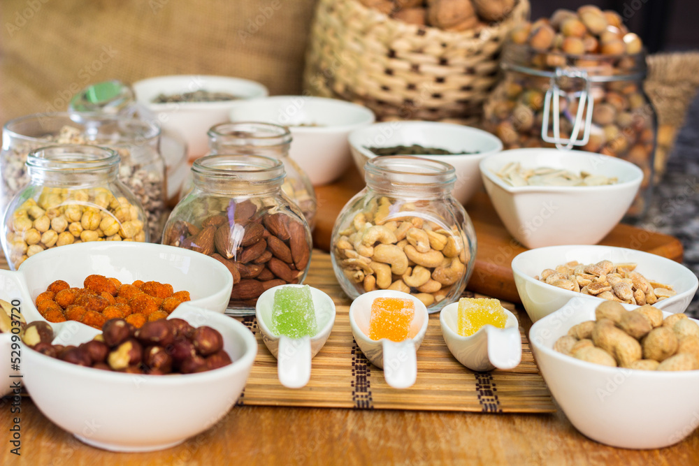 Rustic wood table filled with a large assortment of nuts like pistachios, hazelnut, pine nut, almonds, pumpkin seeds, sunflower seeds, peanuts, cashew and walnuts