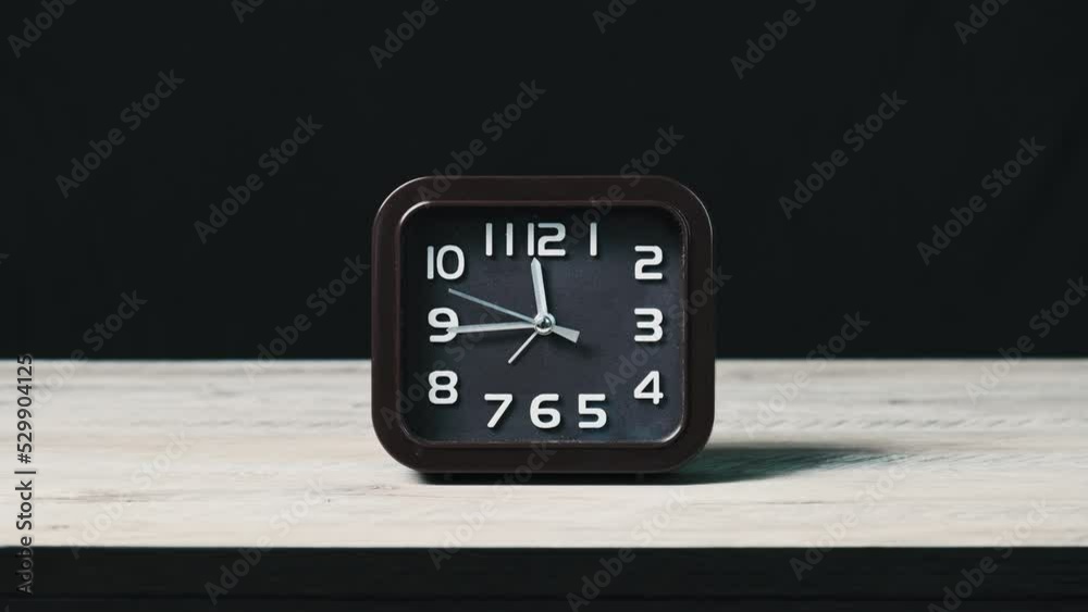 Clock on wooden table and black background show time 12 o'clock. The