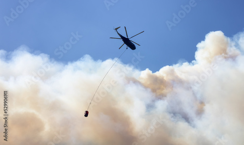 Wildfire Service Helicopter flying over BC Forest Fire and Smoke on the mountain near Hope during a hot sunny summer day. British Columbia, Canada. Natural Disaster