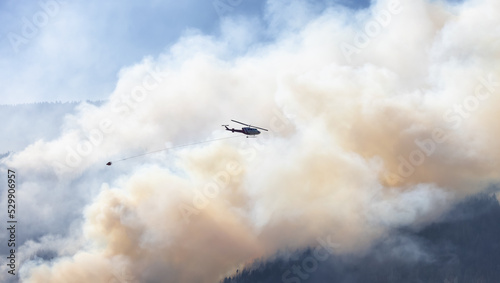 Wildfire Service Helicopter flying over BC Forest Fire and Smoke on the mountain near Hope during a hot sunny summer day. British Columbia, Canada. Natural Disaster