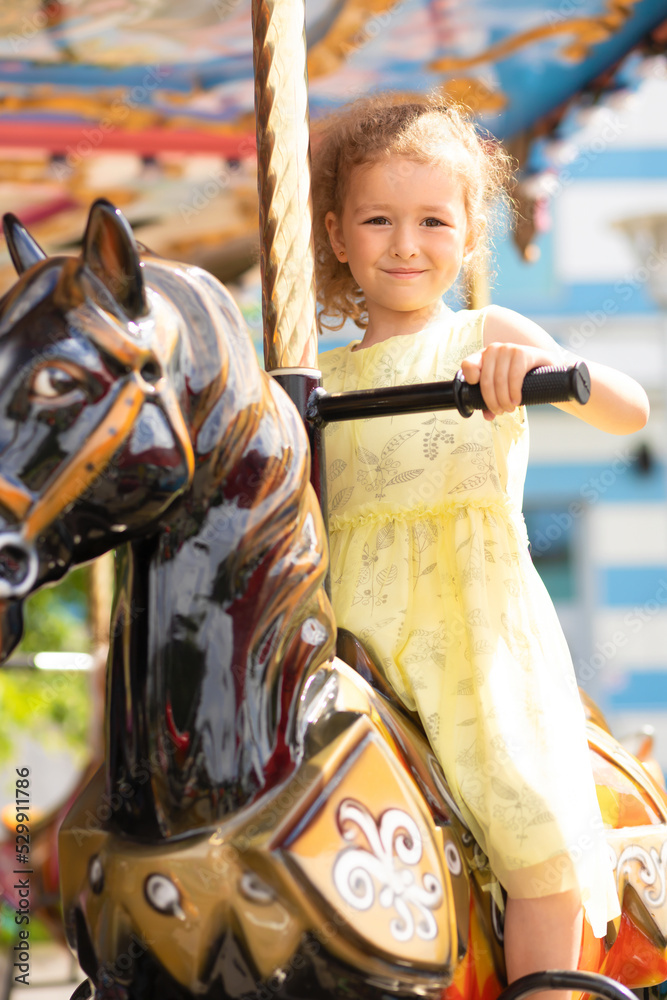 Adorable little toddler girl on carousel horse. child on attraction. kid entertainment. Happy healthy baby having fun outdoor on sunny day. Family weekend, vacations, holiday. vertical