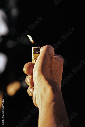 man hand holding lighter with flame on dark background, toned image