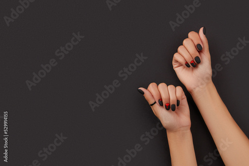 Manicured female hands with fashion accessories on black. Trendy autumn halloween bloody spooky nail design.