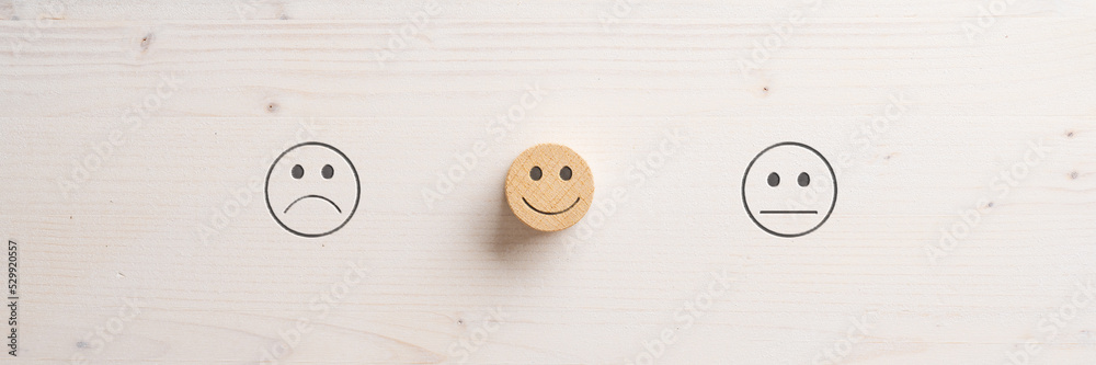 Sad and neutral emoji face symbols cut into wooden background and a smiling one in the middle Sad and neutral emoji face symbols cut into wooden background and a smiling one in the middle