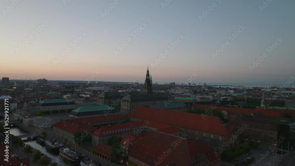 Aerial slide and pan footage of Christiansborg palace with tall tower against colourful twilight sky. Copenhagen, Denmark