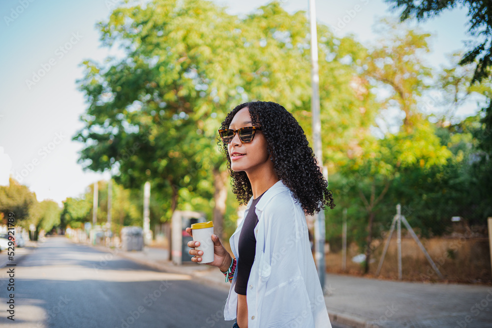 Cheerful black woman having a coffee in the morning while she is walking to work Cheerful black woman having a coffee in the morning while she is walking to work