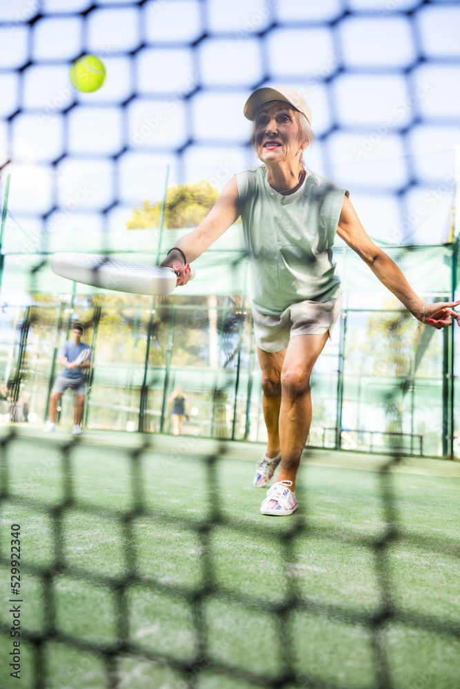 View through the tennis net of an mature female playing padel