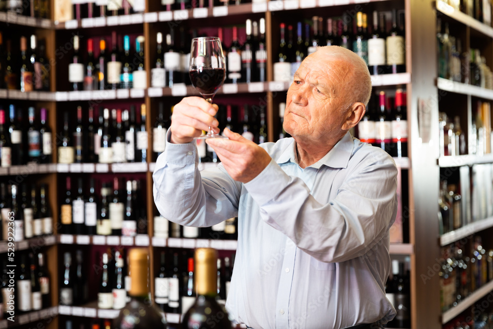 Portrait of senior man tasting red wine at wine shop. High quality photo