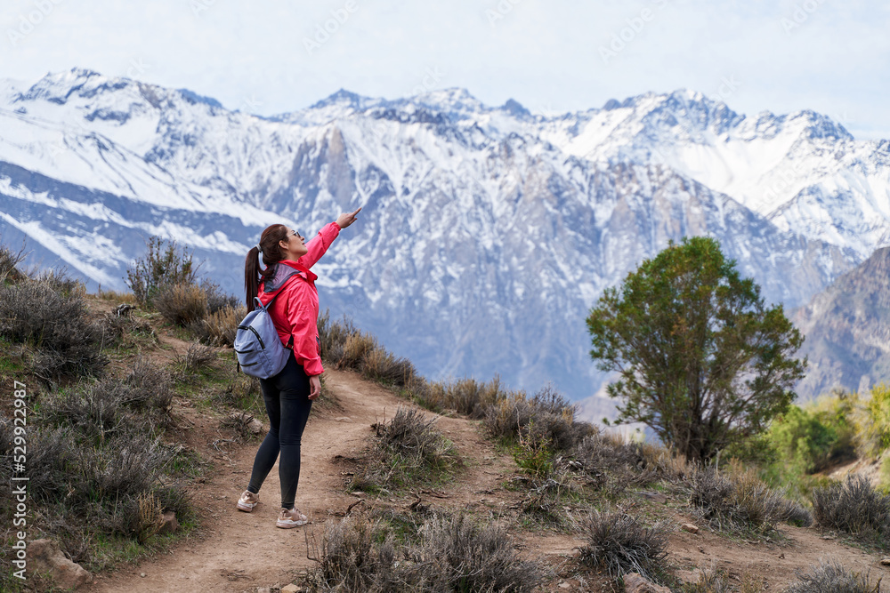 young red haired woman with red jacket and backpack, pointing her finger in the middle of the Andes Mountains of Chile